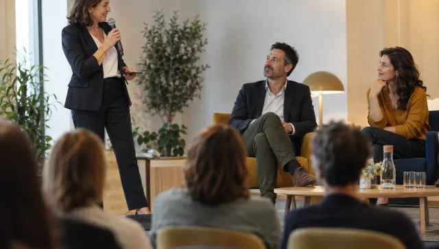 Une animatrice au micro conduit un échange entre deux intervenants sur scène.